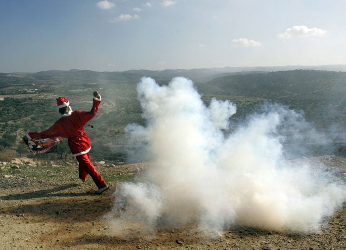 A Palestinian protester wearing a Santa Claus costume runs away from a tear gas canister fired by Israeli troops during a protest against Israel's separation barrier outside the West Bank village of Bilin, near Ramallah, Friday, Dec 24, 2010. (Photo courtesy: AP)