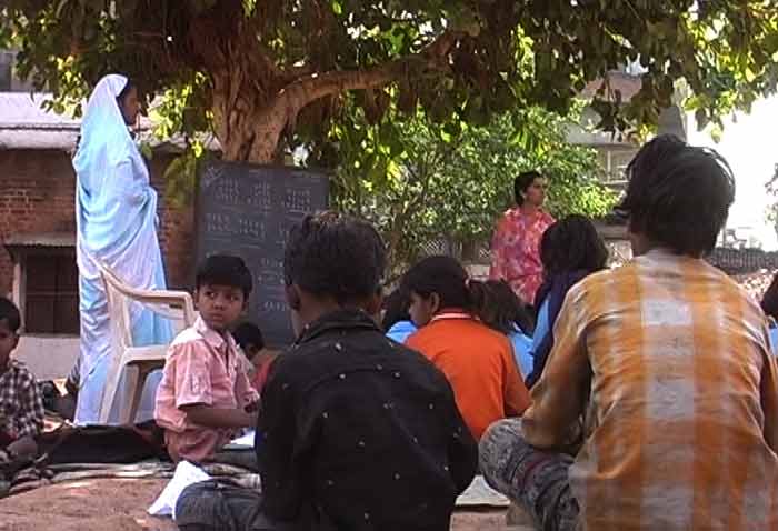 <b>Using every resource</b><br><br>The children being taught in the shadow of a tree as their teachers use the trunk as a makeshift wall to hold the blackboard.