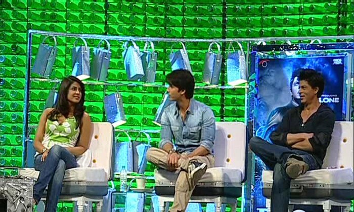 He sits with Priyanka to the left and SRK on the right.