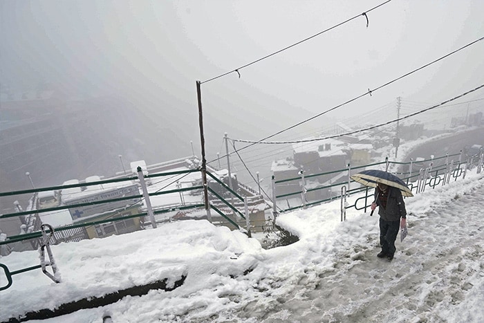 A man walks on a snow-covered road after heavy snowfall, in Shimla on Sunday.