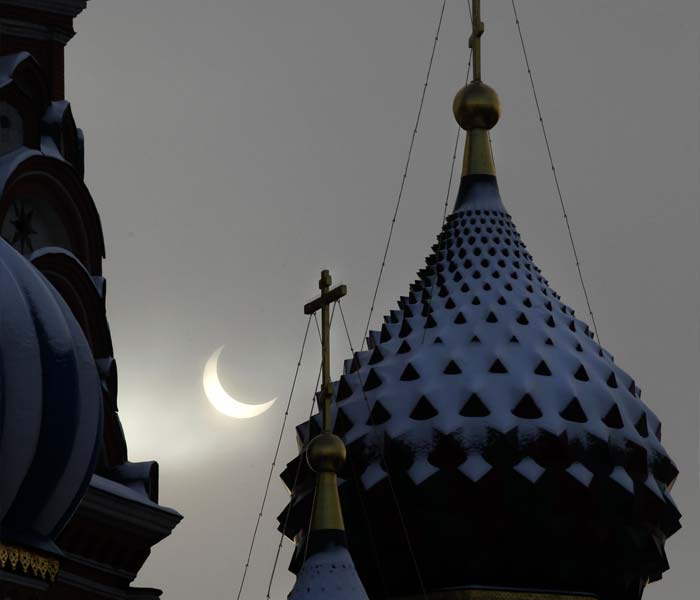 The moon passes in front of the sun, during a partial solar eclipse as snow-covered crosses and domes of St. Bazil's Cathedral are seen in Moscow. (AP Photo)