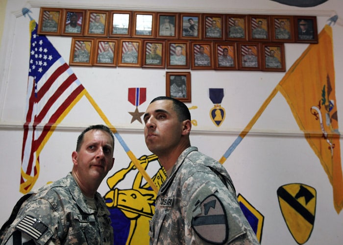 Sergeant John Hyland, left, and Spec. Craig Chavez under portraits of fallen comrades during a visit to Forward Operating Base Normandy in Iraq on October 14, 2009. They are among eight veterans of the war in Iraq who returned this week under a program called Operation Proper Exit, intended to help them heal. (The New York Times)