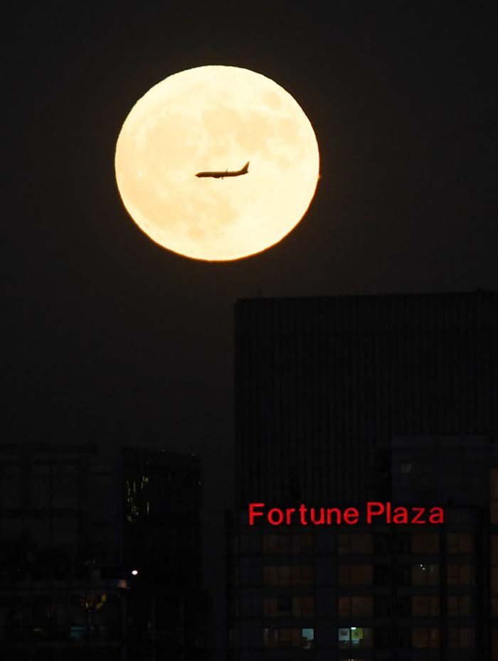 A plane flies past "supermoon" as it rises behind the skyline of Beijing. (AFP Photo)