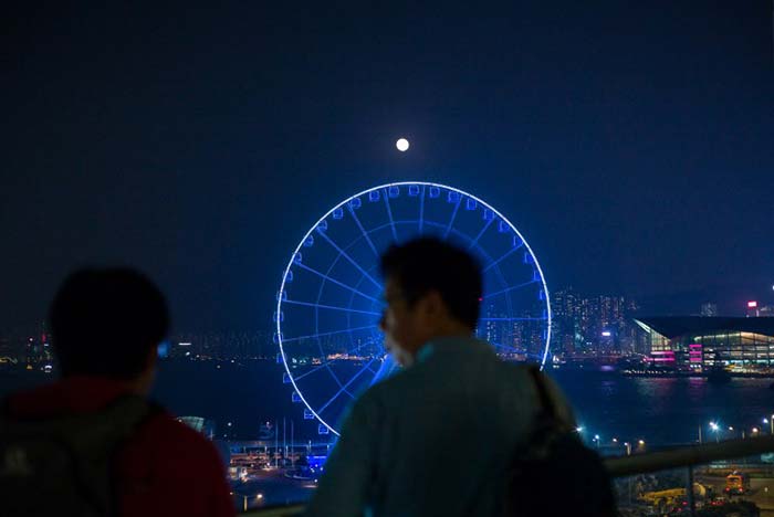 People chat as "supermoon" is seen beyond a ferris wheel in Hong Kong. (AFP Photo)