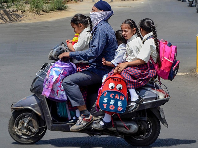 एक व्यक्ति अपने दोपहिया वाहन पर कुछ स्कूली बच्चों के साथ जाते हुए. इस दौरान उन्होंने गर्मी से बचने के लिए अपने चेहरे को कपड़े से ढका हुआ है. (फोटो- पीटीआई)