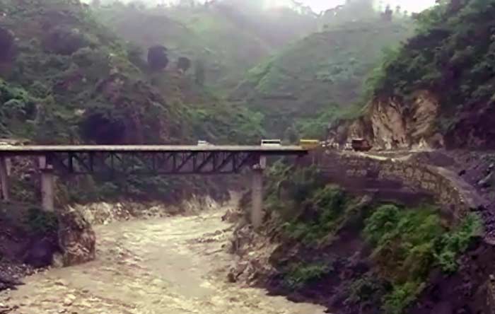 Vehicles navigate perilous roads to crosss a bridge under which a raging river swollen from heavy rains flows