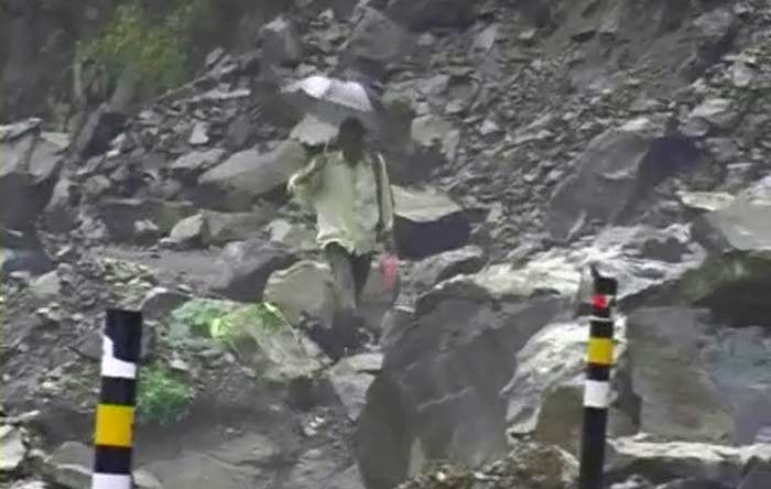 A man holding an umbrella makes his way through a path littered with rocks loosened by the rains