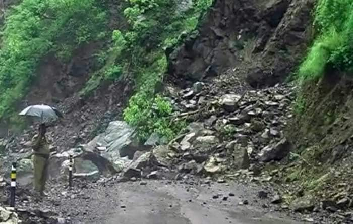 A security personnel shields himself from the heavy rain with an umbrella while surveying a landslide triggered by the incessant rainfall