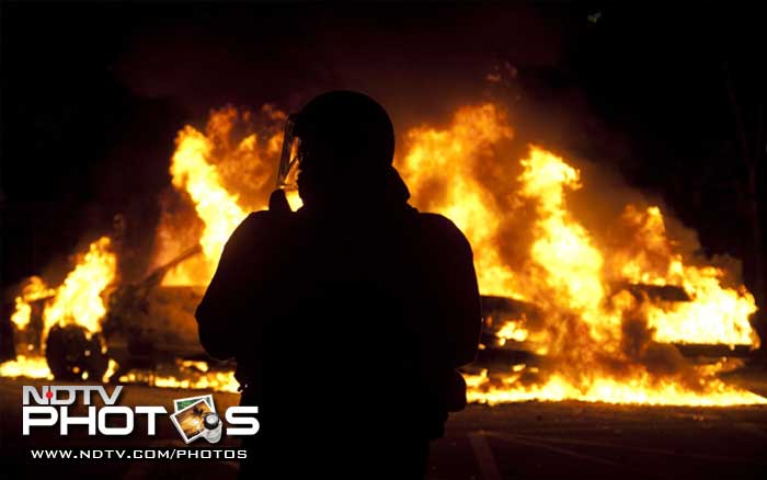 A riot officer watches as two police cars burn during a riot in downtown Vancouver, British Columbia. (AP Photo)