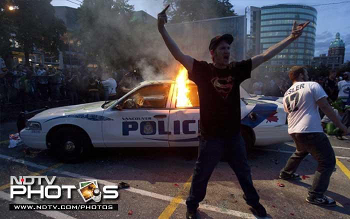 A protestor demonstrates in front of a burning police car during a riot in downtown Vancouver. (AP Photo)