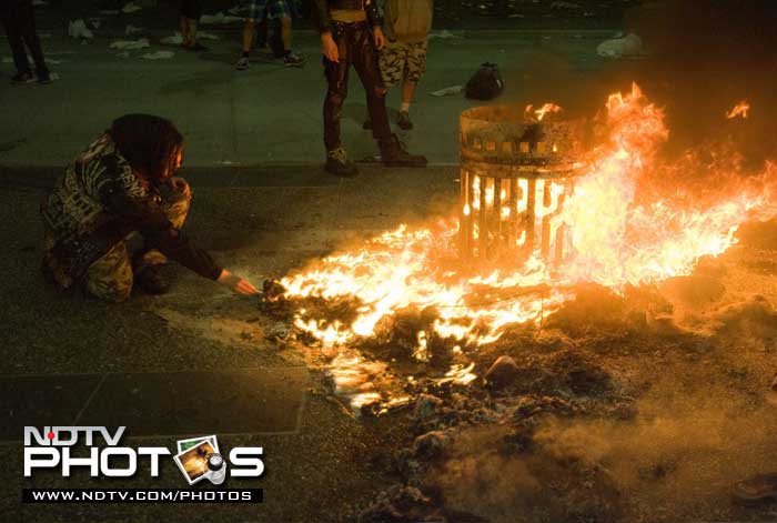 A woman lights her cigarette from a trash can fire during the riot. (AP Photo)