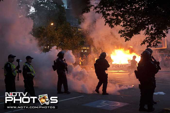 Riot police look on as two police cars burn during a riot in downtown Vancouver. (AP Photo)