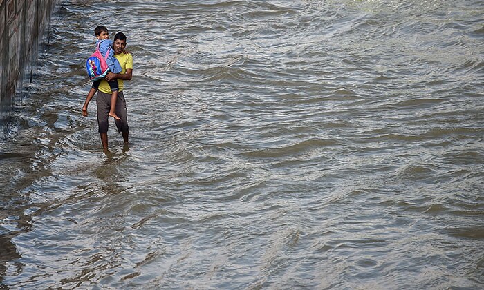 बेंगलुरू में बेलंदूर के पास भारी मानसून की बारिश के बाद पानी से भरे आउटर रिंग रोड से अपने बच्चे को ले जाता एक व्यक्ति. (पीटीआई फोटो/शैलेंद्र भोजक)