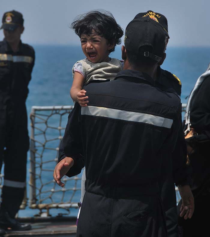 A Naval officer carries a frightened child on board the INS Mumbai during a large scale rescue and evacuation operation of Indian nationals from Yemen's Aden. Photo Courtesy: Indian Navy
