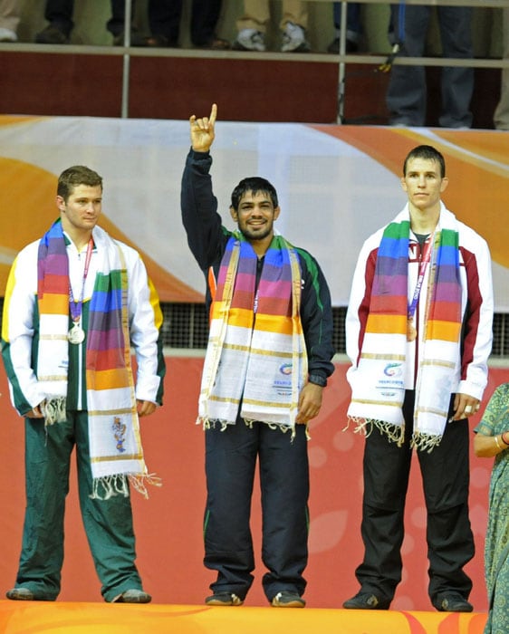 India's Sushil Kumar gestures from the podium as South Africa's Heinrich Barnes and Canada's Chris Prickett (R) look on from the podium during the men's 66 kg wrestling awards ceremony at the Commonwealth Games in New Delhi. Indian world champion Sushil Kumar delighted an expectant home crowd with a gold in the Commonwealth Games freestyle wrestling 66kg. (AFP Photo)