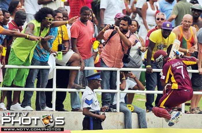 West Indies cricketer Marlon Samuels leaps over the billboard to shake hands with West Indies cricket star Chris Gayle. New look Gayle graces the stands