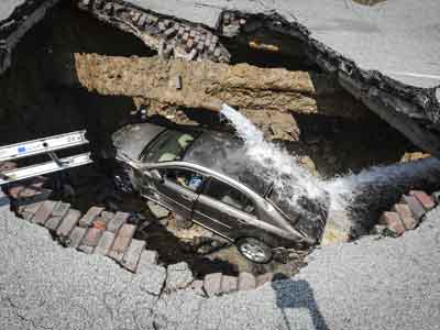 सड़क पर गड्ढे में महिला समेत समा गई कार